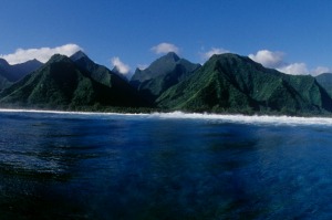 Surfer's view inside a breaking wave with lush green mountain backdrop in Tahiti.